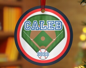 Könnte beinhalten: Runder Weihnachtsbaumschmuck mit einem Baseballfeld-Design. Der Anhänger ist rot, weiß und blau mit einem grünen Baseballfeld und einem Baseball in der Mitte. Der Name "Caleb" ist in blauen Buchstaben oben auf dem Anhänger gedruckt. Das Jahr "2023" ist in weißen Buchstaben unter dem Baseball gedruckt.