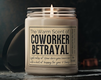 May include: A white candle in a glass jar with a black label that reads "The Warm Scent of Coworker Betrayal". The label also includes the text "Light notes of 'How dare you leave me' with a hint of happy for you & tears".