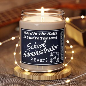 May include: A brown soy wax candle with a white label that reads "Word In The Halls Is You're The Best School Administrator Ever". The candle is lit and sitting on a wooden coaster.