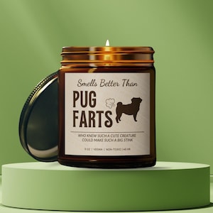 May include: A brown glass candle jar with a black and white illustration of a pug dog. The candle jar has a label that reads "Smells Better Than Pug Farts" and "Who knew such a cute creature could make such a big stink". The candle jar is 9 oz, vegan, non-toxic, and has a 45 hour burn time.