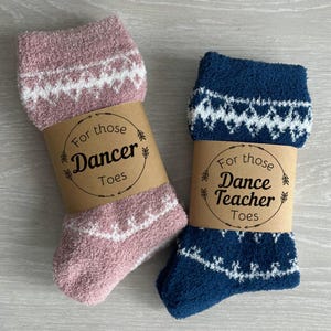 May include: Two pairs of fuzzy socks with decorative labels. The pink socks have a label that says "For those Dancer Toes". The blue socks have a label that says "For those Dance Teacher Toes".