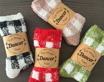 May include: Four pairs of cozy socks in black and white, red and white, pink and white, and green and white checkered patterns. Each pair is wrapped with a brown paper band that reads "For those Dancer Toes."