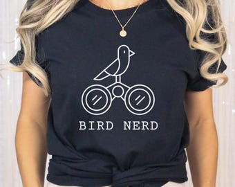 May include: Black t-shirt with a white graphic of a bird perched on binoculars, with the text "BIRD NERD" below. The shirt is a crew neck style.