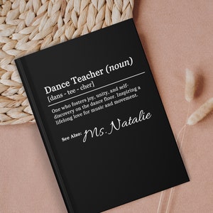 May include: Black notebook with white text that reads "Dance Teacher (noun) [dans - tee - cher] One who fosters joy, unity, and self-discovery on the dance floor. Inspiring a lifelong love for music and movement. See Also: Ms. Natalie"