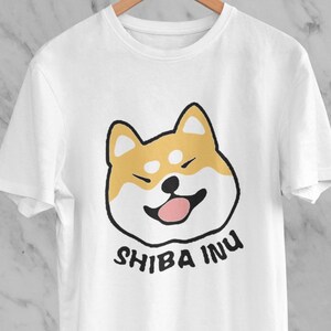 May include: White t-shirt featuring a cartoon Shiba Inu dog graphic and the text "SHIBA INU" printed in black.