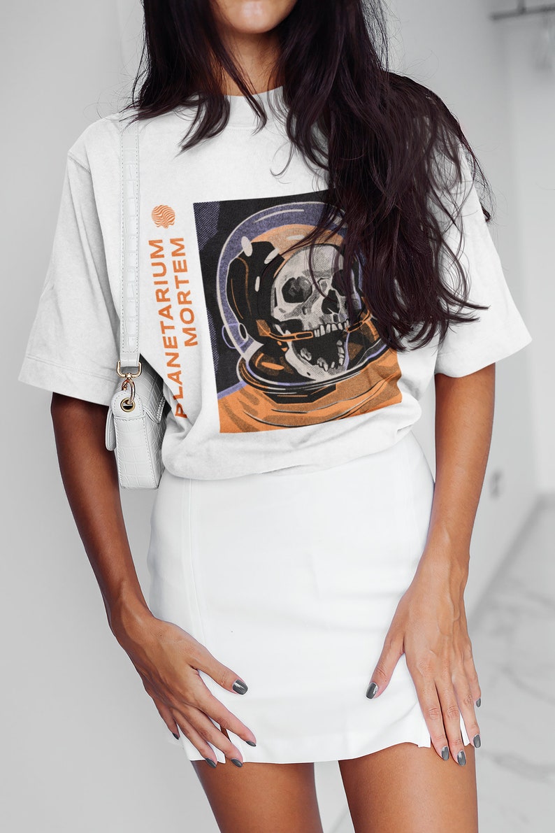 May include: White t-shirt with a graphic print of a skull in a space helmet. The text "PLANETARIUM MORTEM" is printed vertically on the left side of the graphic.