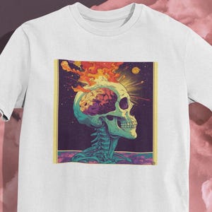 May include: White t-shirt featuring a colorful graphic of a skull with a brain and flames. The skull is in profile, with a teal jawline and neck. The brain is pink and the flames are orange and yellow.