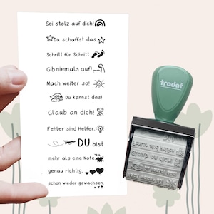 Könnte beinhalten: Ein grüner und schwarzer Stempel mit einem weißen Papier mit deutschem Text und Illustrationen. Der Text enthält Sätze wie "Sei stolz auf dich!" und "Du kannst das!" Der Stempel ist von der Marke Trodat.