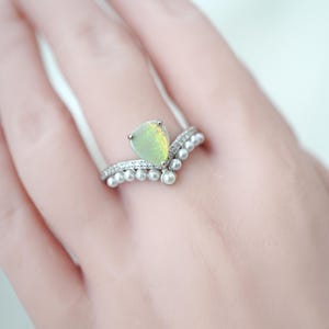 Könnte beinhalten: Ein silberner Ring mit einem birnenförmigen Opal-Edelstein und einem Chevron-Design. Der Ring hat kleine, runde Perlen und winzige klare Steine. Der Opal hat ein hellgrünes und gelbes Schillern.