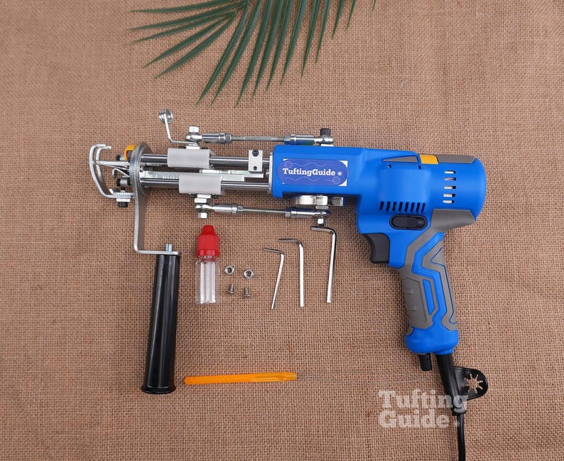 May include: A blue and grey electric tufting gun with a black handle, featuring the text TuftingGuide on the side. Included are a small clear oil bottle with a red cap, two metal nuts, two screws, three L-shaped hex keys, and an orange tool.