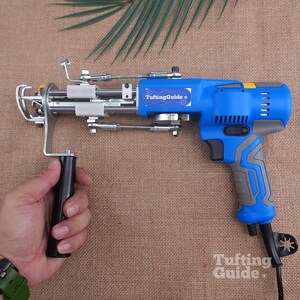 May include: A blue and grey electric tufting gun with a metal needle mechanism and a black handle. The device features a blue label with the white text TuftingGuide and a small white star icon. The tool includes a black power cord and a trigger.