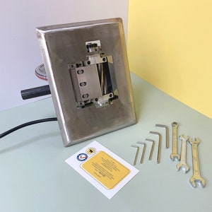 May include: A stainless steel machine with a roller and a black cord. The machine is on a light green surface. There are several wrenches and Allen wrenches on the surface next to the machine.