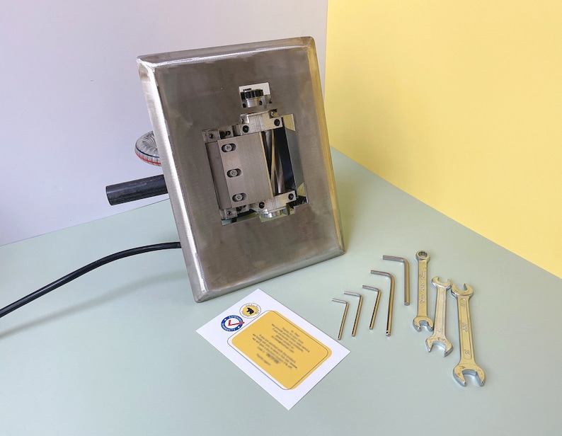 May include: A stainless steel machine with a roller and a black cord. The machine is on a light green surface. There are several wrenches and Allen wrenches on the surface next to the machine.