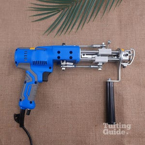 May include: A blue and grey electric tufting gun with a black handle, metal mechanical components, and a power cord. The device features a trigger mechanism, ventilation slots on the motor housing, and the text Tufting Guide printed in white.
