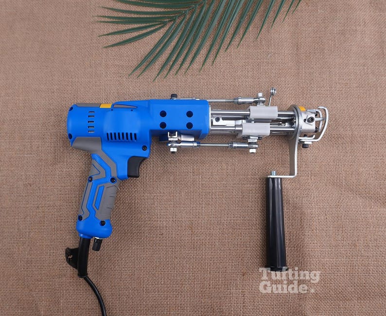 May include: A blue and grey electric tufting gun with a black handle, metal mechanical components, and a power cord. The device features a trigger mechanism, ventilation slots on the motor housing, and the text Tufting Guide printed in white.