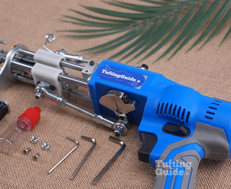 May include: A blue and grey electric tufting gun with a metal needle mechanism, featuring a TuftingGuide label. Included are a small clear oil bottle with a red cap, two metal nuts, two screws, and three L-shaped hex keys for assembly and maintenance.
