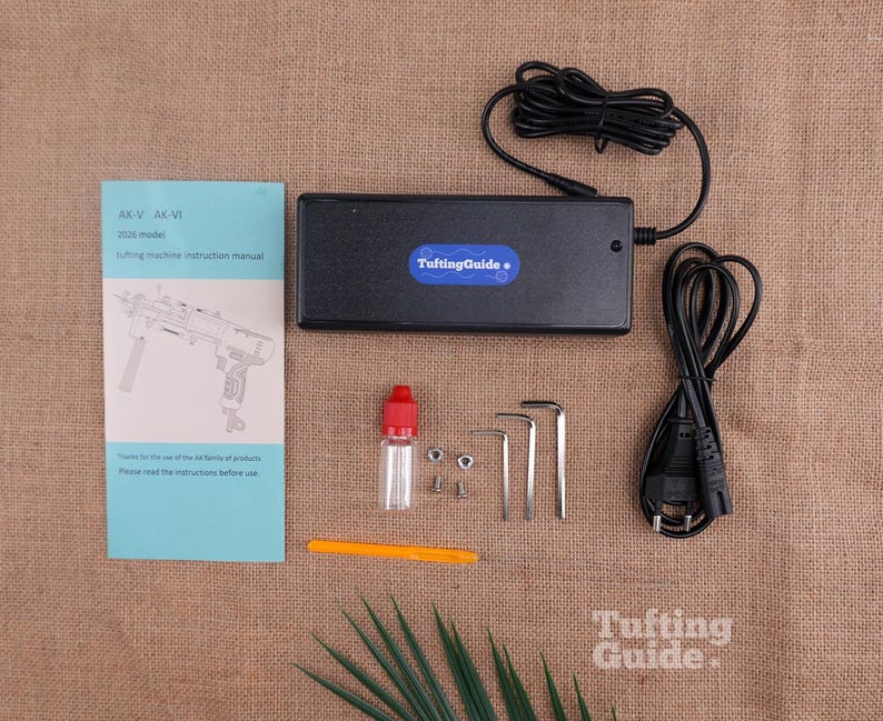 May include: A black power adapter with a TuftingGuide label, a light blue instruction manual for AK-V and AK-VI models, a small clear bottle with a red cap, two metal nuts, two screws, three L-shaped hex keys, an orange tool, and a black power cord.
