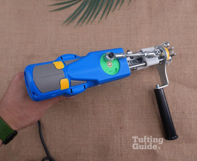 May include: A blue and grey electric tufting gun with yellow accents, a green circular gear component, a silver metal needle mechanism, and a black handle. The device features a white plastic part near the needle and a black power cord.