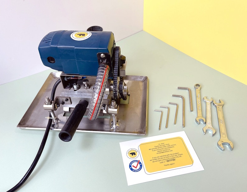 May include: A blue and silver electric glass grinder with a black hose and a set of wrenches and Allen keys. The grinder has a yellow sticker with a bear logo.