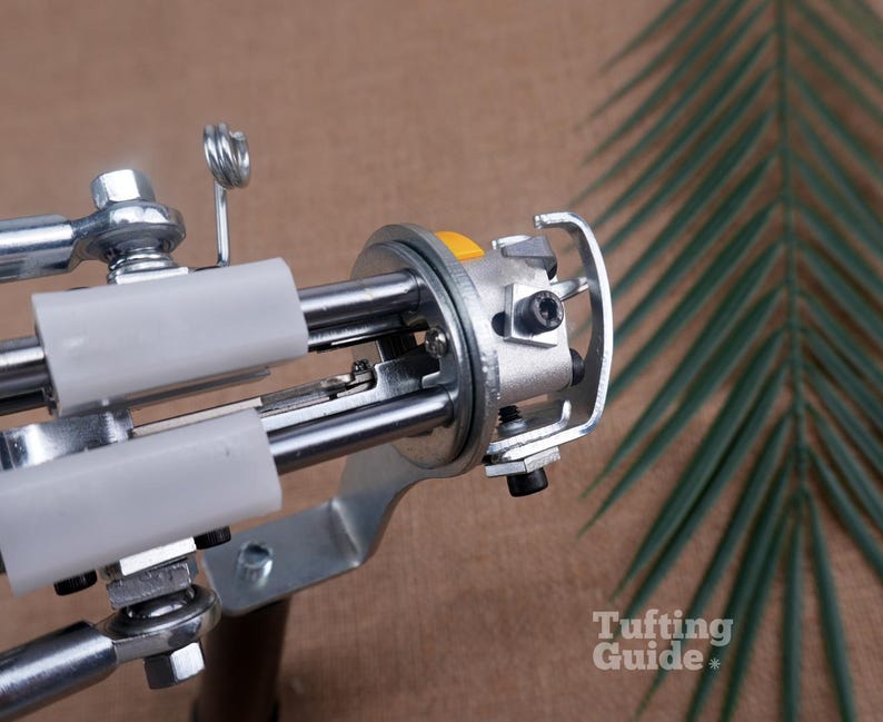 May include: A metal tufting gun mechanism featuring a silver-toned frame, two white plastic guide tubes, a yellow button, and exposed mechanical components including screws and a hook. The text Tufting Guide is visible in the bottom right corner.