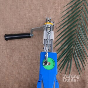 May include: A blue and silver tufting gun featuring a black handle, a green circular gear component, and a metal needle mechanism. The device includes a silver metal arm and a white plastic housing. The text Tufting Guide is visible.