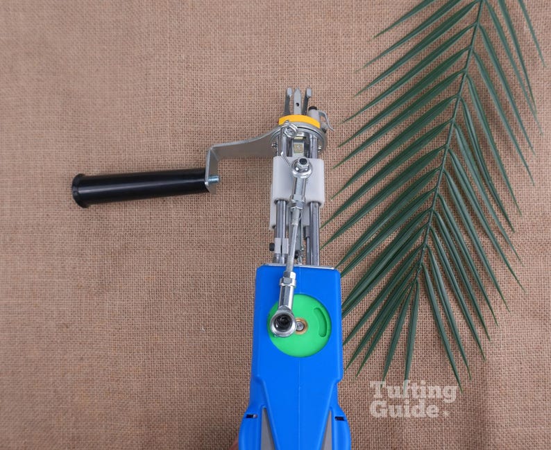 May include: A blue and silver tufting gun featuring a black handle, a green circular gear component, and a metal needle mechanism. The device includes a silver metal arm and a white plastic housing. The text Tufting Guide is visible.