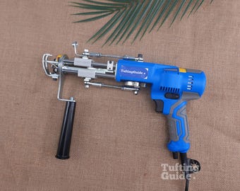 May include: A blue and grey electric tufting gun featuring a black handle, a metal needle mechanism, and a label that reads TuftingGuide. The power tool has a trigger, ventilation slots, and a power cord extending from the bottom of the grip.