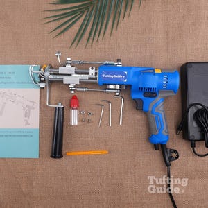 May include: A blue and grey electric tufting machine with a metal needle mechanism, a black handle, a power adapter with a cord, a small oil bottle, three L-shaped hex keys, a yellow tool, and an instruction manual labelled AK-V AK-VI 2026 model.