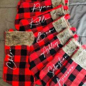 May include: Set of red and black buffalo plaid Christmas stockings with faux fur trim and personalized names: Abby, Ryan, Kelli, Ben, Ashley, Sebastian, Brennan, and Chloe.