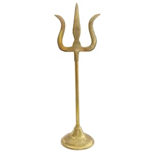 May include: A gold-colored trident statue with three curved prongs and a long, slender stem. The trident sits on a round, decorative base. The statue is made of metal and stands upright against a white background.