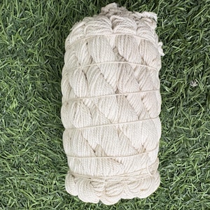 May include: A tightly wound bundle of off-white rope, secured with several horizontal wraps. The rope is thick and appears to be made of natural fibers. The bundle is resting on a bed of green grass.