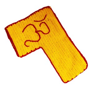 Könnte beinhalten: Handgefertigtes gelbes Häkelteil mit rotem Rand und rotem Om-Symbol. Der Artikel hat eine einzigartige Form und ist wahrscheinlich ein dekoratives Stück oder eine kleine Matte. Die Häkelarbeit ist detailliert und die Farben sind lebendig.