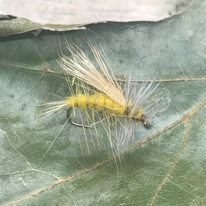 May include: A yellow and white fly fishing lure with a hook and feathers.