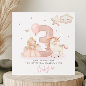 May include: A square birthday card featuring a large pink number three, a cartoon princess, and a unicorn. The text reads: HAPPY 3RD BIRTHDAY TO A VERY SPECIAL GRANDDAUGHTER, followed by the name Isabelle in pink script with a small butterfly.