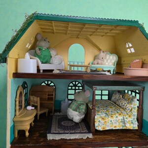 K&ouml;nnte beinhalten: Ein mehrst&ouml;ckiges Puppenhaus mit gr&uuml;nem Dach und gelben W&auml;nden. Das Haus ist mit Miniaturm&ouml;beln eingerichtet und enth&auml;lt M&auml;usefiguren. Das Puppenhaus hat ein Bett, ein Sofa, einen Schminktisch und anderes Zubeh&ouml;r. Das Haus ist etwa 30 cm hoch.