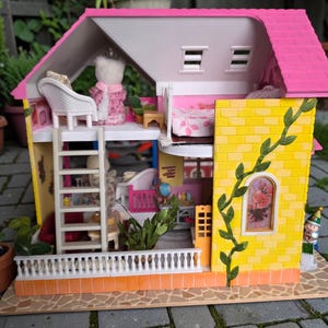 May include: A colorful dollhouse with a pink roof, yellow brick walls, and a white balcony. The dollhouse has multiple levels, a ladder, and a small figure on the balcony. A green vine climbs up the side.