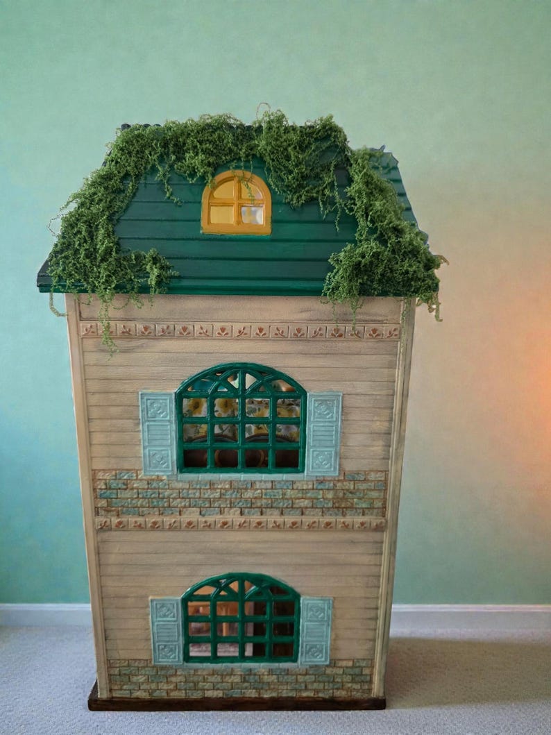 K&ouml;nnte beinhalten: Ein Holzpuppenhaus mit gr&uuml;nem Dach und kleinem gelben Fenster. Das Haus hat zwei gr&uuml;ne Bogenfenster mit blauen Fensterl&auml;den. Die Fassade ist in hellen Holzt&ouml;nen mit Ziegelakzenten gehalten.