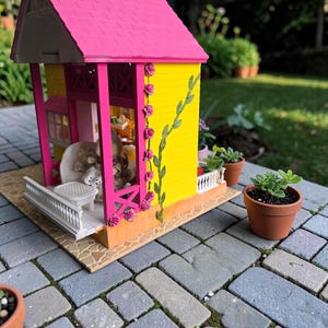 May include: A miniature dollhouse with a bright pink roof and yellow walls. The house has a porch with a white railing and is decorated with pink roses and green vines. Small potted plants sit nearby on a brick patio.