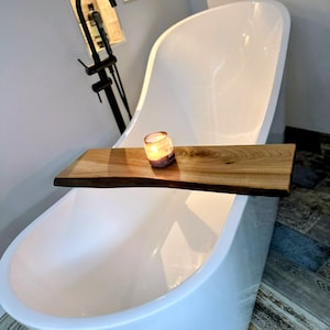 May include: A white, modern bathtub with a wooden bath tray. A lit candle sits on the tray. The bathroom has a black faucet and a neutral color scheme. The wooden tray is approximately 24 inches long.