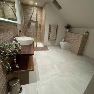 K&ouml;nnte beinhalten: Ein modernes Badezimmer mit neutraler Farbpalette. Es verf&uuml;gt &uuml;ber eine begehbare Dusche, einen schwebenden Holzwaschtisch mit einem Steinwaschbecken und eine Toilette. Die W&auml;nde sind mit einem Holzmaserungsmuster gefliest, der Boden ist hellgrau gefliest.