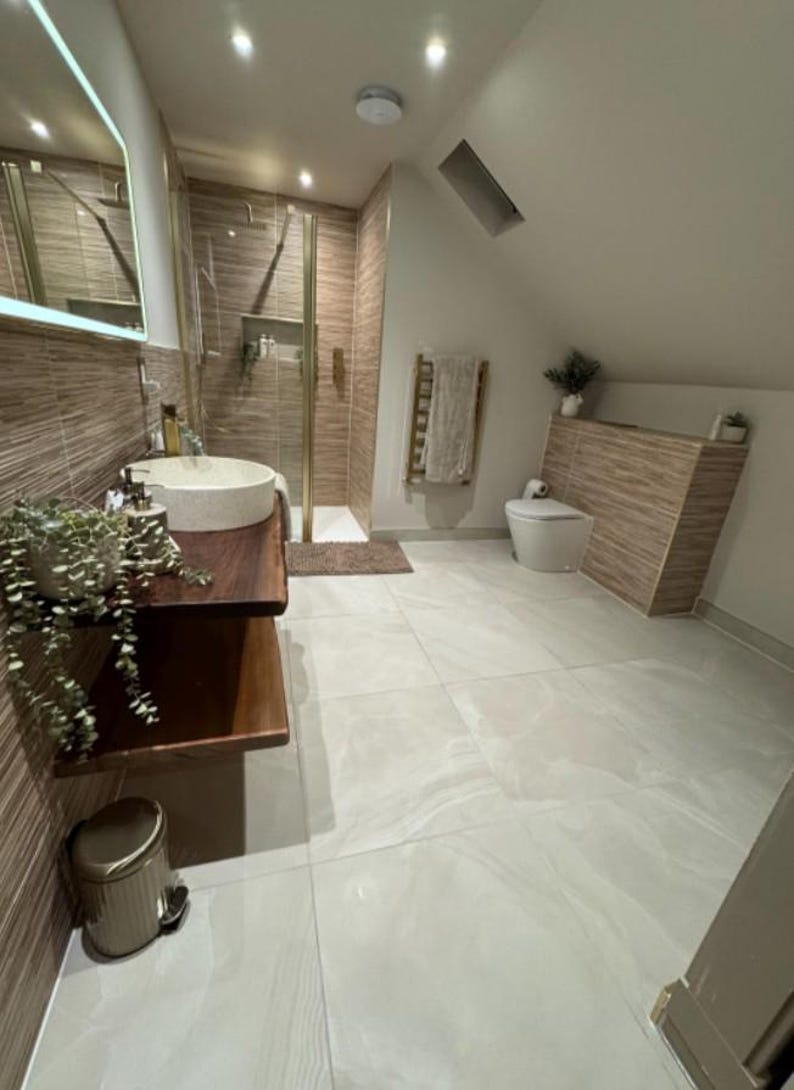 K&ouml;nnte beinhalten: Ein modernes Badezimmer mit neutraler Farbpalette. Es verf&uuml;gt &uuml;ber eine begehbare Dusche, einen schwebenden Holzwaschtisch mit einem Steinwaschbecken und eine Toilette. Die W&auml;nde sind mit einem Holzmaserungsmuster gefliest, der Boden ist hellgrau gefliest.