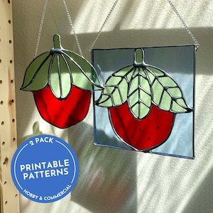 May include: Two stained glass strawberry ornaments, each with a red body and green leaves, suspended by silver chains. One is square, the other is strawberry-shaped. A blue circle displays "2 Pack Printable Patterns Hobby & Commercial."