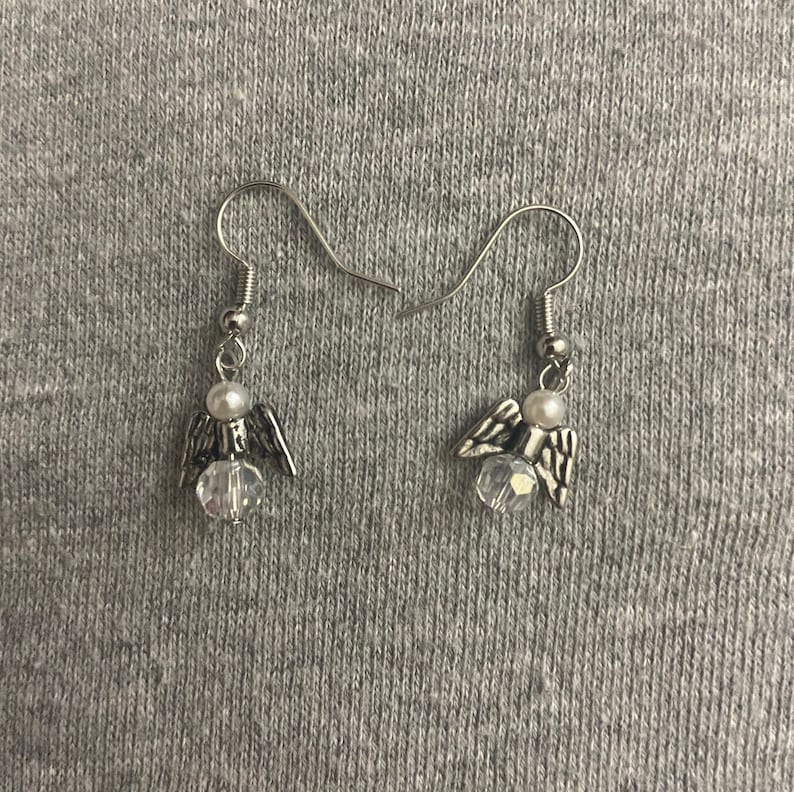 Puede incluir: Un par de pendientes de &aacute;ngel de plata con un cristal transparente y una perla blanca en cada pendiente.