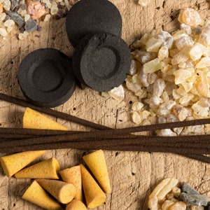 May include: A close-up of incense sticks, charcoal briquettes, and resin crystals. The incense sticks are brown and have a natural wood scent. The charcoal briquettes are black and round. The resin crystals are clear and have a yellow tint.