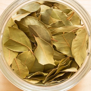 May include: A glass jar filled with dried bay leaves. The leaves are a light brown colour and have a slightly wrinkled texture.