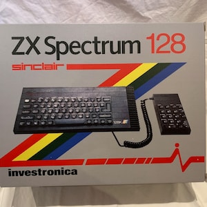 May include: A gray box with the text "ZX Spectrum 128" in black and "sinclair" in white. The box features a black and gray computer with a keyboard and a black joystick. The box also has a black and gray keypad with a coiled cord. The box has a red, yellow, blue, and green stripe design. The text "investornica" is printed in black at the bottom of the box.