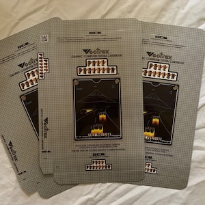 Puede incluir: Tres cajas de cartuchos de juego grises para la consola de videojuegos Vectrex. Cada caja presenta una imagen en blanco y negro del juego "Poly-Play" con el texto "Vectrex Graphic Computer System Cartridge" y "Poly-Play".
