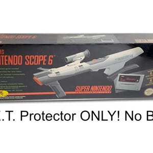 Op de afbeelding: Een wit en grijs Super Nintendo Nintendo Scope 6-accessoire in de originele doos. De doos heeft de tekst "Super NES Nintendo Scope 6" en "Super Nintendo Entertainment System".