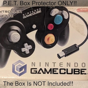 Puede incluir: Mando negro de Nintendo GameCube sobre una caja con el texto "P.E.T. Box Protector ONLY!!" y "The Box Is NOT Included!!". El mando tiene botones de colores y un cable.