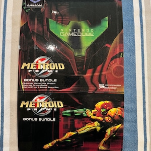 Peut inclure: Un coffret bonus Metroid Prime pour la Nintendo GameCube. La boîte présente le logo Metroid Prime, une illustration de personnage et le logo Nintendo GameCube. La boîte est principalement noire, rouge et verte.